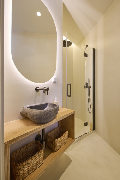 Modern bathroom at Casa Redonda Aroeira with stone vessel sink, backlit oval mirror, rainfall showerhead, and wooden vanity