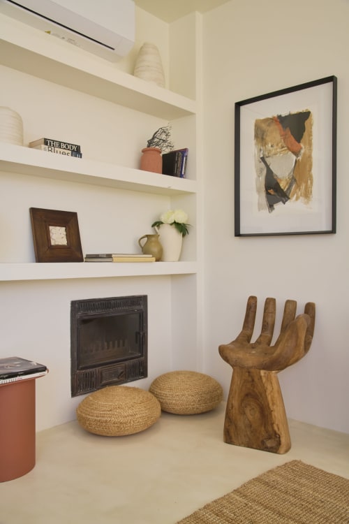 Modern apartment alcove with wooden hand sculpture, woven poufs, fireplace, and framed artwork at Casa Redonda