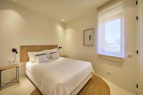 Modern bedroom at Casa Redonda Aroeira with white bedding, rattan headboard, pool view window, and natural lighting