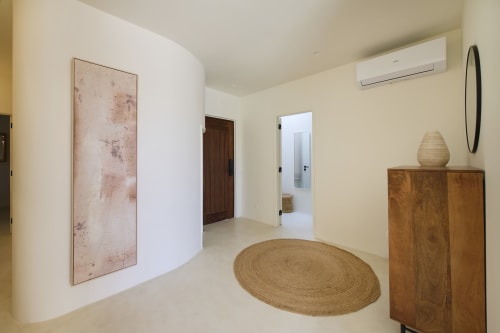 Modern entryway of Casa Redonda apartment in Aroeira with circular jute rug, wooden dresser, and abstract artwork