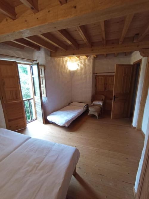 Amplia sala familiar en Casa Aldea L'Ayalga en Infiesto con vigas de madera, múltiples camas y vistas al jardín desde puertas abiertas