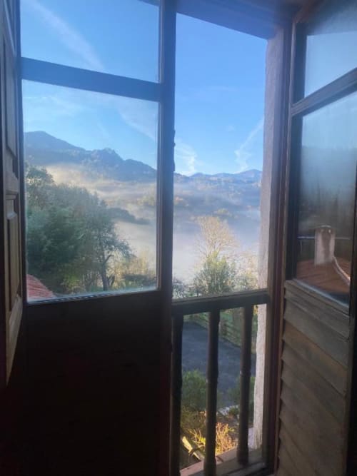 Vista del valle montañoso a través de las puertas dobles abiertas de la habitación doble de Casa Aldea L'Ayalga en Infiesto
