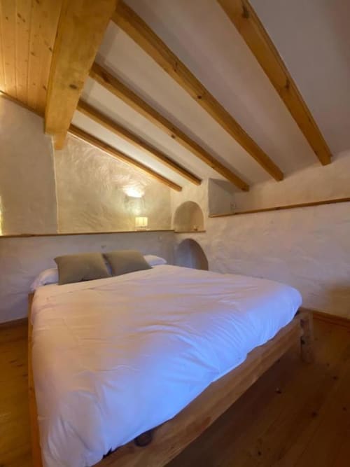 Acogedor dormitorio en Casa Aldea L'Ayalga con techo de vigas de madera, ropa de cama blanca e iluminación cálida