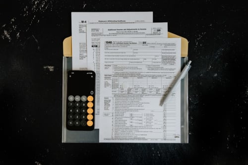 Steuerformulare W-4, 1040 und Anlage 1 mit Taschenrechner und Stift auf dunkler Oberfläche
