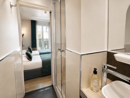 Salle de bains moderne avec douche vitrée à l'Hôtel des Bains, vue sur la chambre avec panorama sur la ville