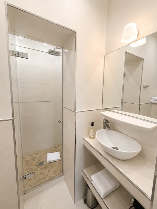Salle de bains moderne de la chambre Supérieure de l'Hôtel des Bains avec douche vitrée, vasque et finitions en carrelage neutre