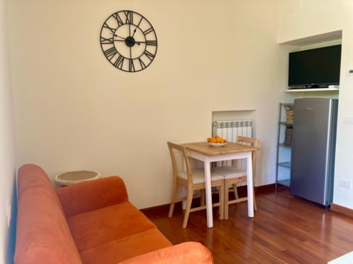 Accogliente zona living dell'appartamento Crawford Home con divano arancione, tavolo da pranzo, frigorifero in acciaio, orologio da parete e TV