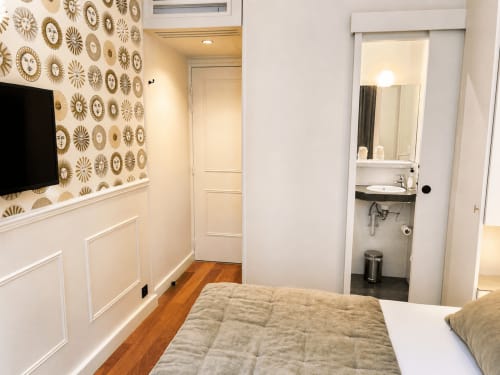 Chambre accueillante à l'Hôtel des Bains avec papier peint à motifs de soleils dorés, TV écran plat, parquets et salle de bain attenante