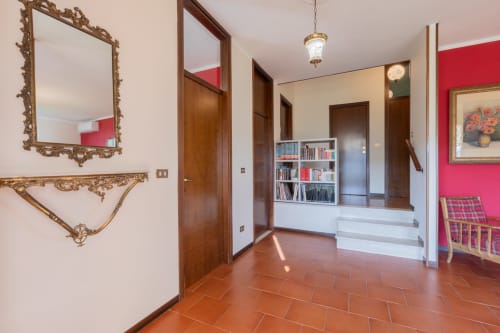 Elegante corridoio di Palazzo Garda Salò con pavimenti in terracotta, specchio dorato ornamentale, porte in legno, libreria e parete rossa accento