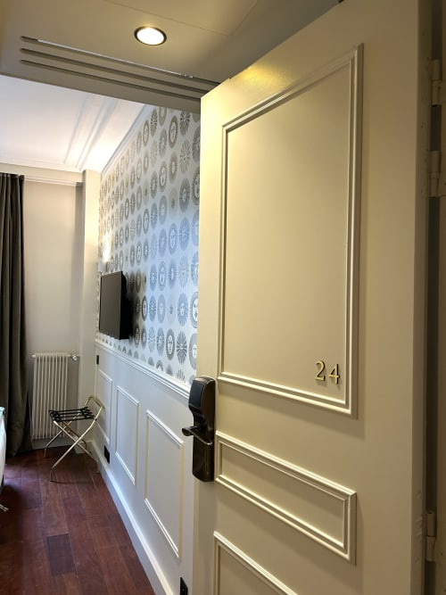 Porte de la chambre 24 de l'Hôtel des Bains avec lambris crème, papier peint motifs et éclairage moderne