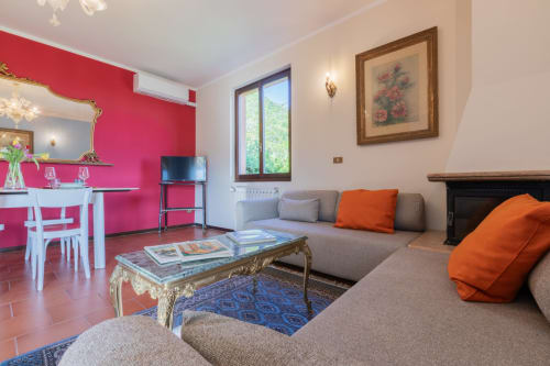 Luminosa sala dell'Hotel Prince Garda a Salò con parete rosa, divano grigio, cuscini arancioni e arredi eleganti