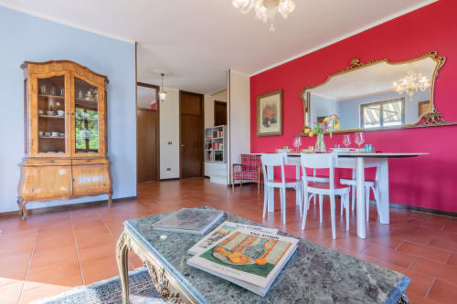 Luminosa zona living e pranzo a Prince Garda Salò con pareti rosse, arredi in legno e tavolo bianco moderno