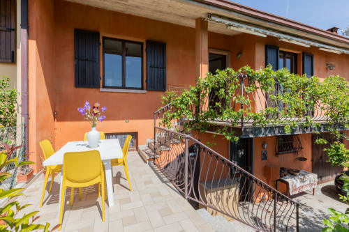 Terrazza Prince Garda a Salò con sedie gialle, tavolo da pranzo e lussureggiante verde su edificio arancione