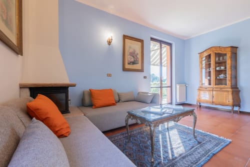 Elegante soggiorno dell'hotel Prince Garda a Salò con pareti blu, divano grigio, cuscini arancioni, camino e vista sul lago
