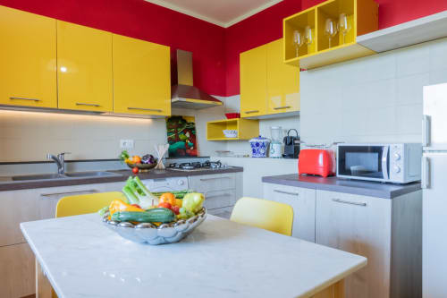 Cucina moderna dell'Hotel Prince Garda a Salò con mobili gialli, pareti rosse e verdure fresche sul tavolo da pranzo