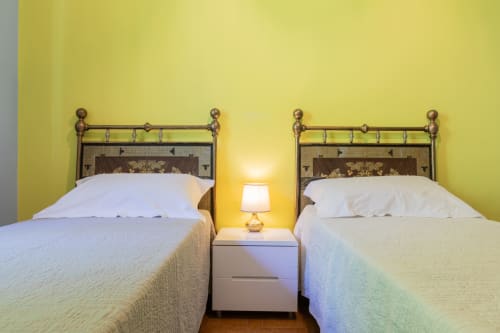 Due letti singoli con testata in ottone in una luminosa camera gialla presso l'Hotel Prince Garda di Salò