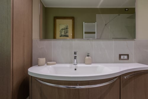 Bagno moderno dell'hotel Prince Garda a Salò con lavabo bianco curvo, mobili in legno e specchio
