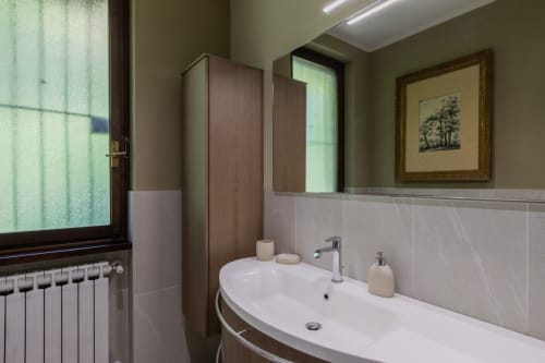 Bagno moderno dell'hotel Prince Garda a Salò con lavabo bianco curvo, piastrelle grigie, porte in legno e finestra con radiatore