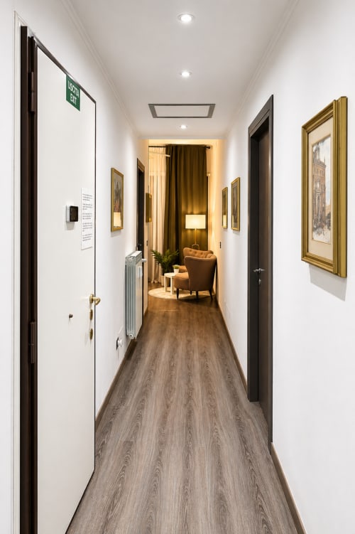 Corridoio moderno a Vatican Living Rome con pavimentazione in legno, opere d'arte incorniciate e ingresso dorato nell'appartamento romano.