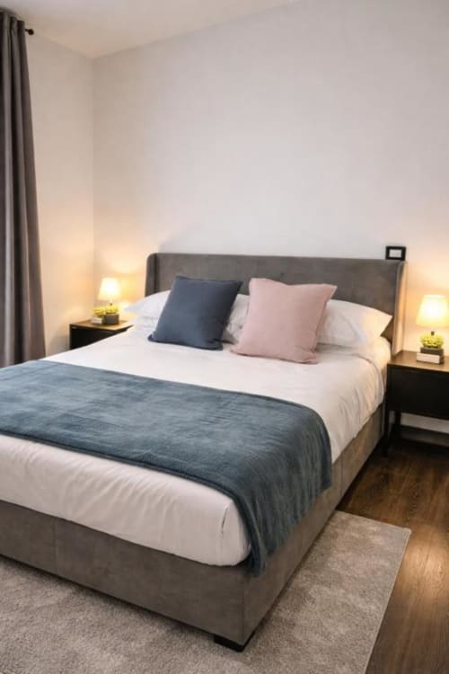 Camera moderna presso Vatican Living Rome con letto rivestito in grigio, biancheria bianca, cuscini decorativi, lampade comodino e legno