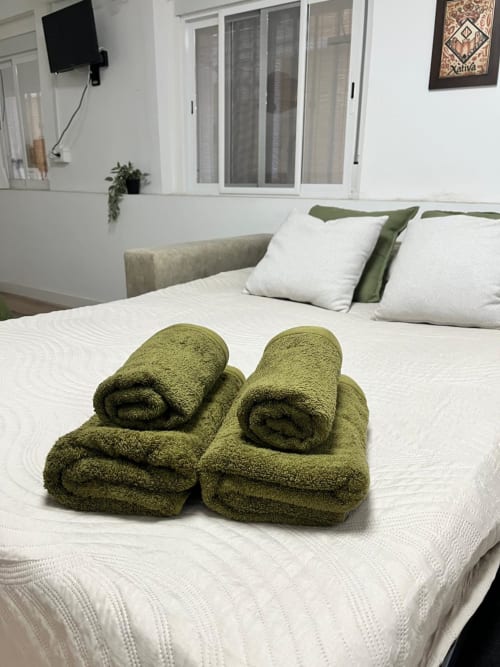 Toallas enrolladas en verde oliva sobre cama blanca en apartamento Casa Portalet, Xátiva, España