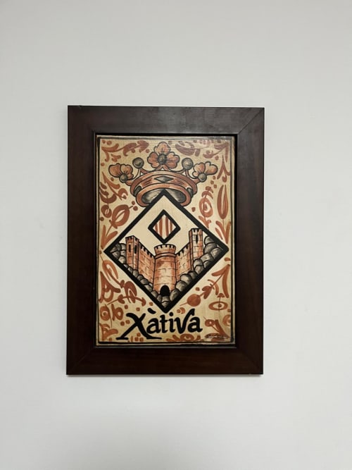 Escudo heráldico enmarcado de Xàtiva con ornamentación elaborada y emblema de torre castillo en marco de madera oscura