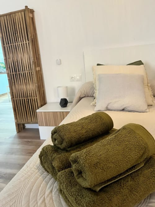 Acogedora habitación en Casa Portalet en Xativa con toallas de oliva enrolladas sobre cama crema y biombo de madera