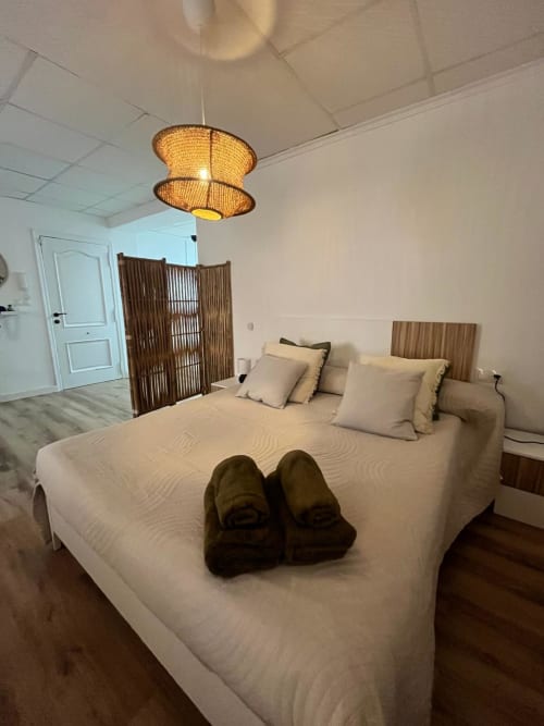 Dormitorio moderno en Casa Portalet, apartamento Xativa con ropa de cama beige, lámpara colgante tejida, mamparas de madera y piso de madera