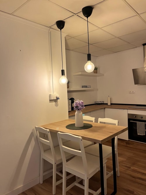 Comedor moderno en Casa Portalet, Xativa con mesa de madera, sillas blancas, lámparas colgantes y cocina equipada