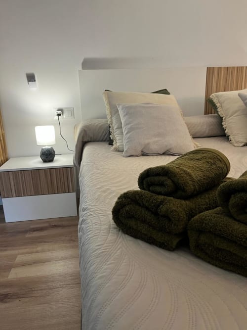 Dormitorio moderno en apartamento Casa Portalet en Xátiva con cama queen, toallas verde oliva enrolladas, lámpara de mesita y madera