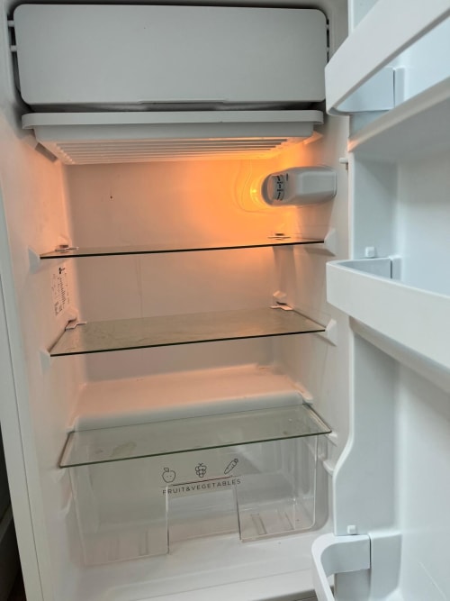 Interior del refrigerador abierto en el apartamento Casa Portalet, Xátiva, mostrando estantes vacíos y cajón de frutas y verduras