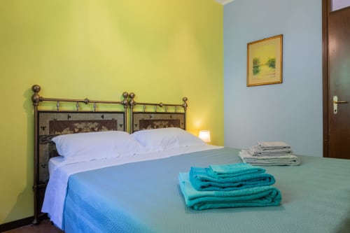 Camera luminosa dell'Hotel Prince Garda a Salò con pareti gialle e blu, struttura in metallo e asciugamani freschi