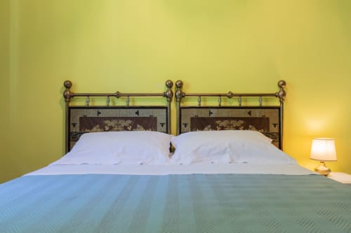 Camera da letto dell'Hotel Prince Garda a Salò con letto in ottone, cuscini bianchi, coperta blu e pareti gialle