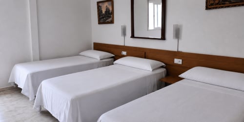 Habitación triple limpia en el Hostal Europa de Aldaia con tres camas individuales, cabecero de madera, espejo y ropa de cama blanca