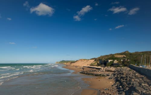 Plage de sable avec côte rocheuse, vagues turquoise et falaises sableuses aux Logis d'Emma, France