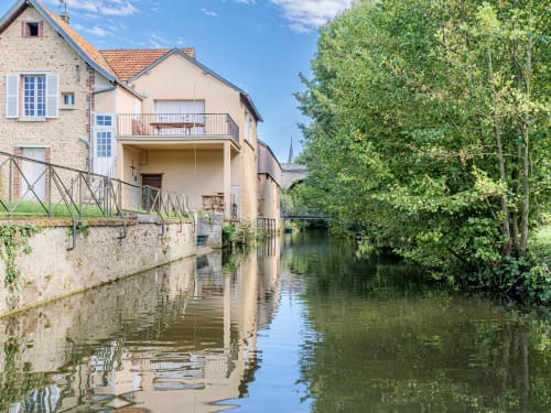 L'hôtel Les Logis d'Emma en bord de canal avec ses bâtiments en pierre, terrasse et arbres luxuriants se reflétant dans l'eau calme