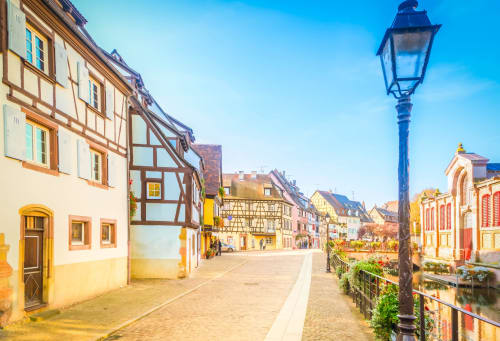 Charmante rue à colombages en Alsace avec bâtiments historiques, lampadaire bleu et hôtel Les Logis d'Emma