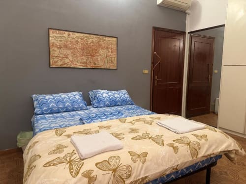 Camera da letto BnB Fantasia Bologna con letto blu decorato, piumone farfalla, quadri geografici e porte in legno scuro
