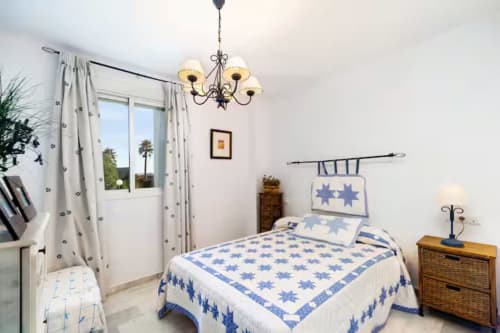 Habitación luminosa en Barrosa Home con ropa de cama azul con estrellas, araña, cortinas estampadas y vistas costeras