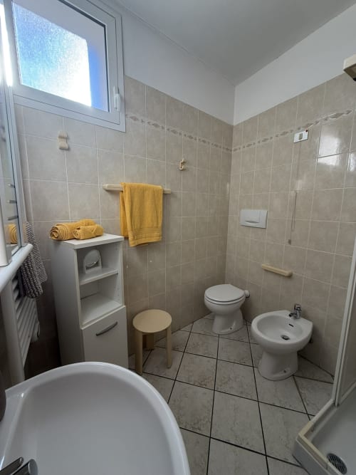 Bagno moderno con WC, bidet, lavabo e asciugamani gialli presso l'appartamento Agriturismo Gli Ulivi, pareti con piastrelle beige