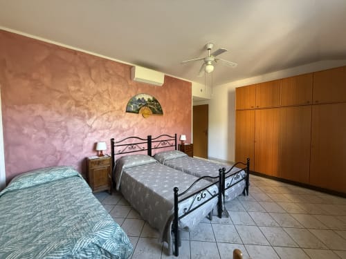 Camera spaziosa all'Agriturismo Gli Ulivi con tre letti, muri in terracotta, armadio in legno e pavimenti in cotto
