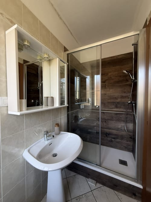 Modern bathroom with pedestal sink, illuminated mirror cabinet, and walk-in shower with wood-look tiles at Agriturismo Gli