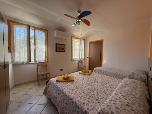 Spacious bedroom at Agriturismo Gli Ulivi with two beds, ceiling fan, windows, and wooden furnishings