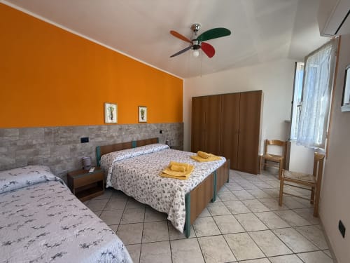Spacious bedroom at Agriturismo Gli Ulivi with two beds, orange accent wall, colorful ceiling fan, and terracotta tile