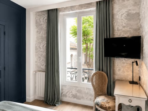 Chambre Deluxe de l'Hôtel des Bains avec vue sur jardin, portes-fenêtres, rideaux verts et mobilier moderne
