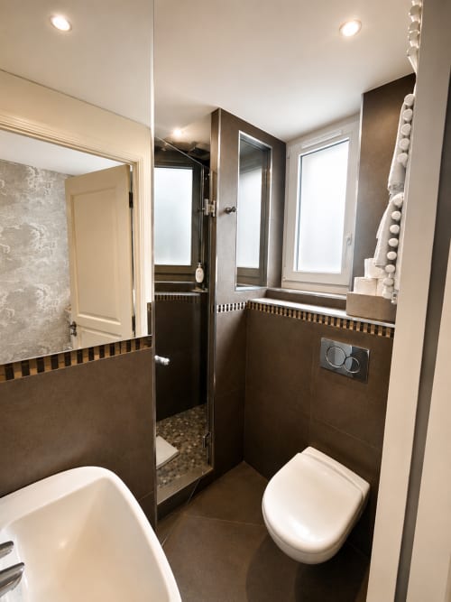 Salle de bain moderne dans une chambre Deluxe à l'Hôtel des Bains avec carrelage foncé, douche à effet pluie, toilettes et éclairage lumineux
