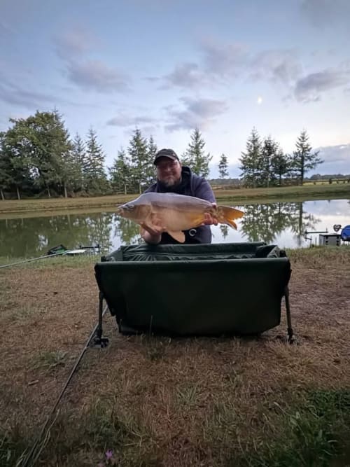 Fisherman holds large carp at Les 5 Etangs pond in Brinon-sur-Sauldre, France