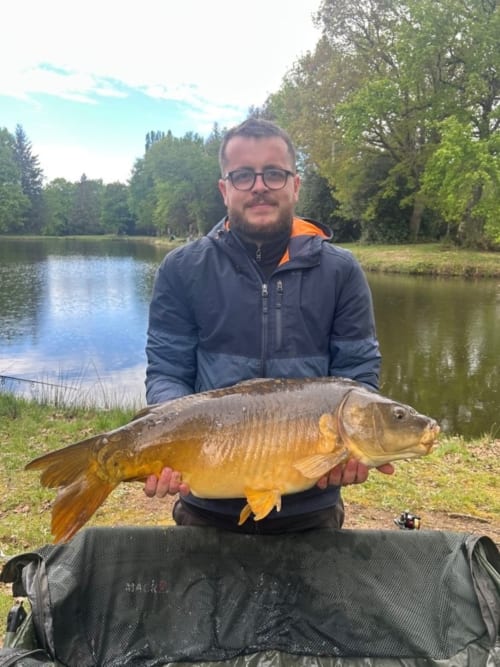 Man holding large carp by pond at Les 5 Etangs, fishing destination in Brinon-sur-Sauldre, France
