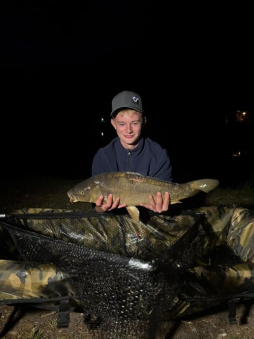 Young angler holding a large carp at Les 5 Etangs fishing pond in Brinon-sur-Sauldre, France