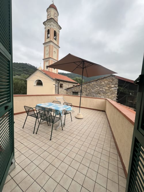 Terrazza con tavolo da pranzo e ombrellone con vista sulla torre della chiesa, Agriturismo Gli Ulivi, Toscana